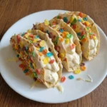 Fruity Pebbles Cheesecake Tacos on a white ceramic dessert plate with creamy filling and uneven cereal coating
