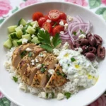 Greek Chicken Bowl with rice chicken vegetables feta and tzatziki on a white plate