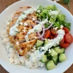 Greek Chicken Gyro Bowl with browned chicken and rice and vegetables and tzatziki on a white plate
