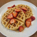 Homemade Belgian Waffles on a speckled white plate with maple syrup and strawberries