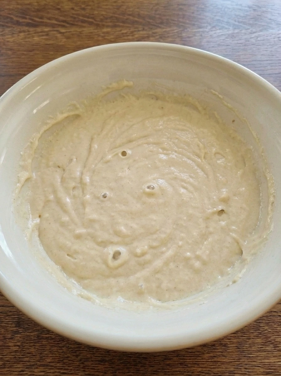 Rested waffle batter with small bubbles in a ceramic bowl