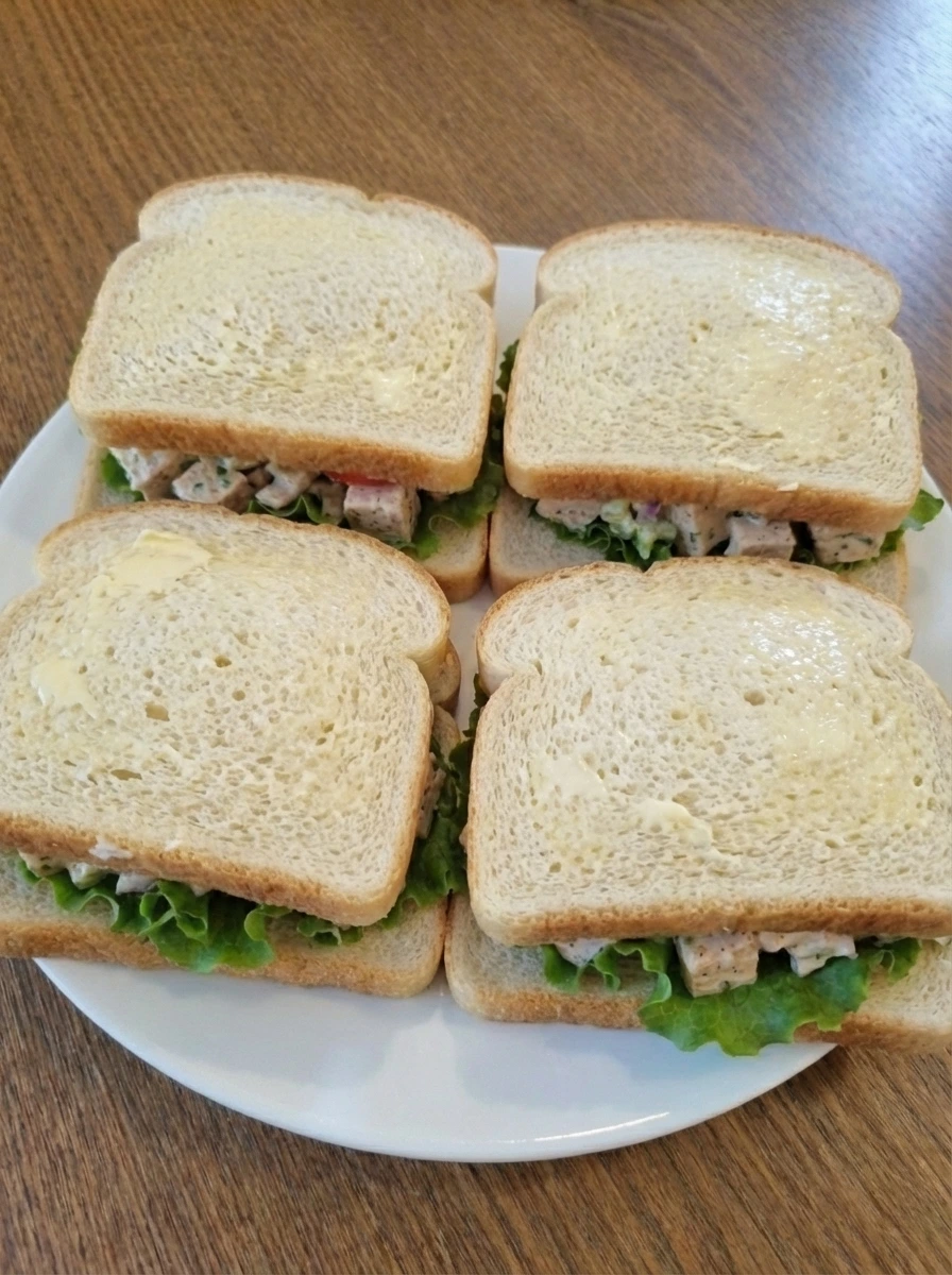 Closed chicken salad sandwiches with buttered bread ready to toast