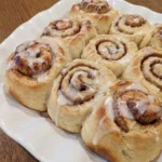 Homemade Cinnamon Rolls on a round white stoneware plate with creamy icing and golden brown swirls