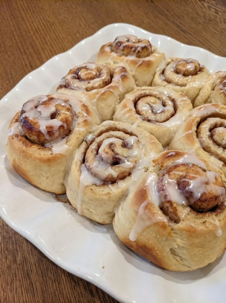 Homemade Cinnamon Rolls on a round white stoneware plate with creamy icing and golden brown swirls