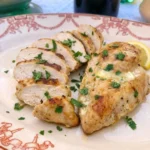 Juicy baked chicken breast on a white stoneware plate with parsley and lemon