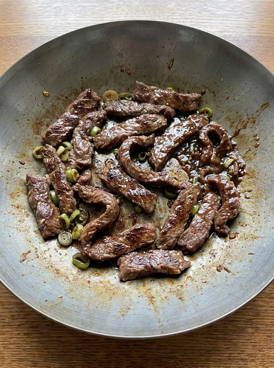 Bulgogi beef cooking with glossy sauce and browned edges in a wok