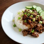 Korean Ground Beef Bowl with rice browned beef cucumber green onions and sesame seeds on a white plate