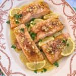 Lemon Garlic Baked Salmon plated on a white oval ceramic plate with glossy sauce and uneven golden brown edges