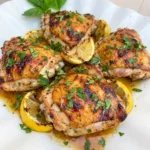 Lemon Herb Grilled Chicken Thighs on a white plate with herbs and lemon wedges.