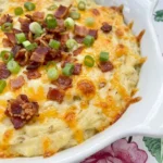Loaded Baked Potato Dip in a white ceramic dish with melted cheddar bacon and green onions.