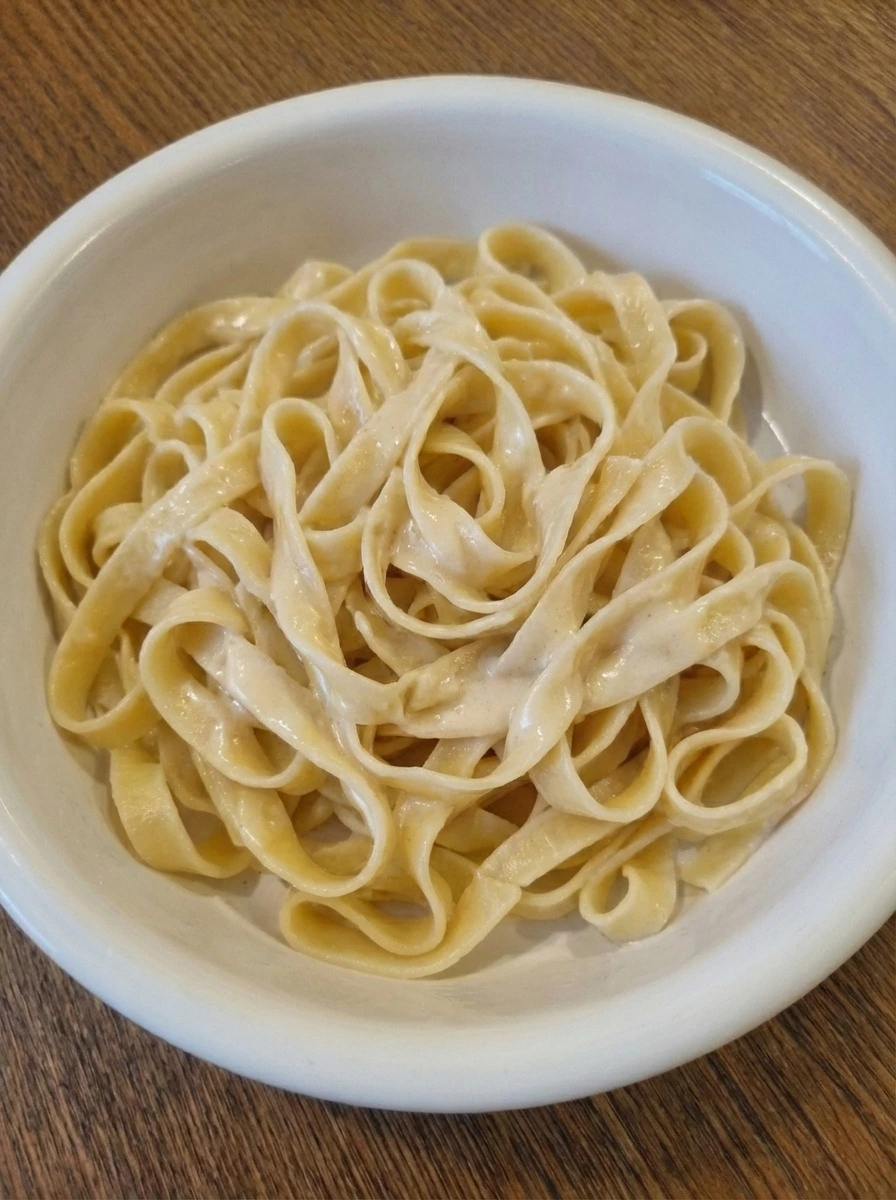 Fettuccine folded into creamy Alfredo sauce on a white dish