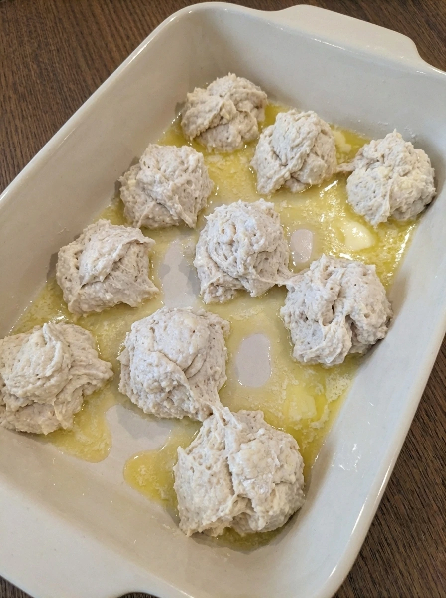 Biscuit dough layered over melted butter in baking dish