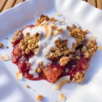 Raspberry Colada baked dessert served warm on a white plate with golden coconut topping and coconut cream drizzle