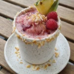Raspberry Pina Colada Cocktail in a speckled white tumbler with toasted coconut and fruit garnish