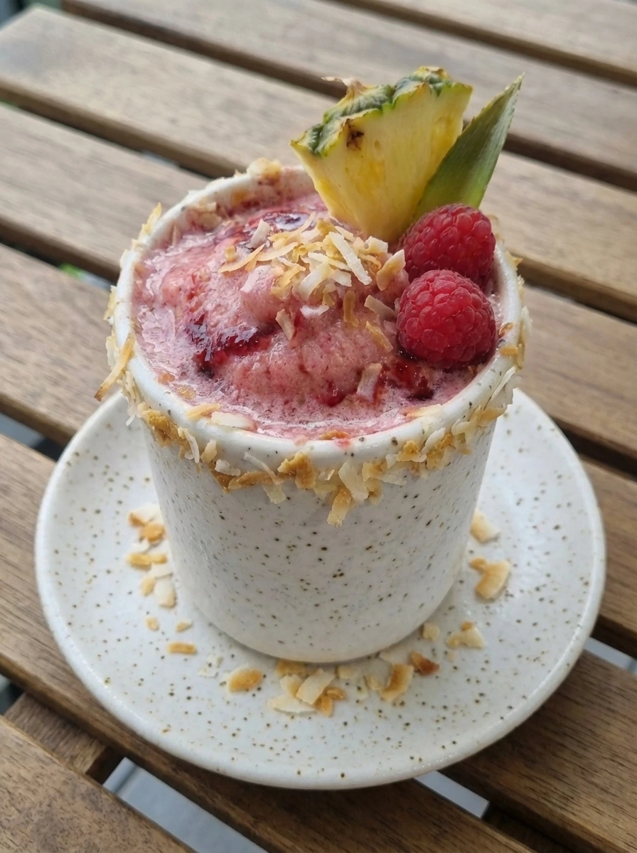 Raspberry Pina Colada Cocktail in a speckled white tumbler with toasted coconut and fruit garnish