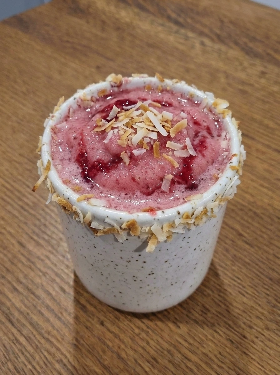 Frozen Raspberry Pina Colada poured into a coconut rimmed tumbler