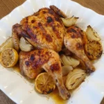 Roast Chicken with Crispy Skin on an oval white stoneware platter with roasted onions and lemon