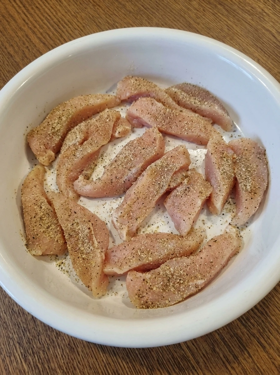 Seasoned chicken strips loosely spread on a white dish for Alfredo pasta