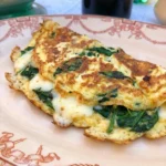 Spinach Cheese Omelette on a white ceramic coupe plate with melted cheese and browned edges