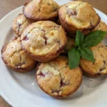 Strawberry Cream Cheese Muffins on a rustic round white ceramic plate with golden tops and creamy swirls