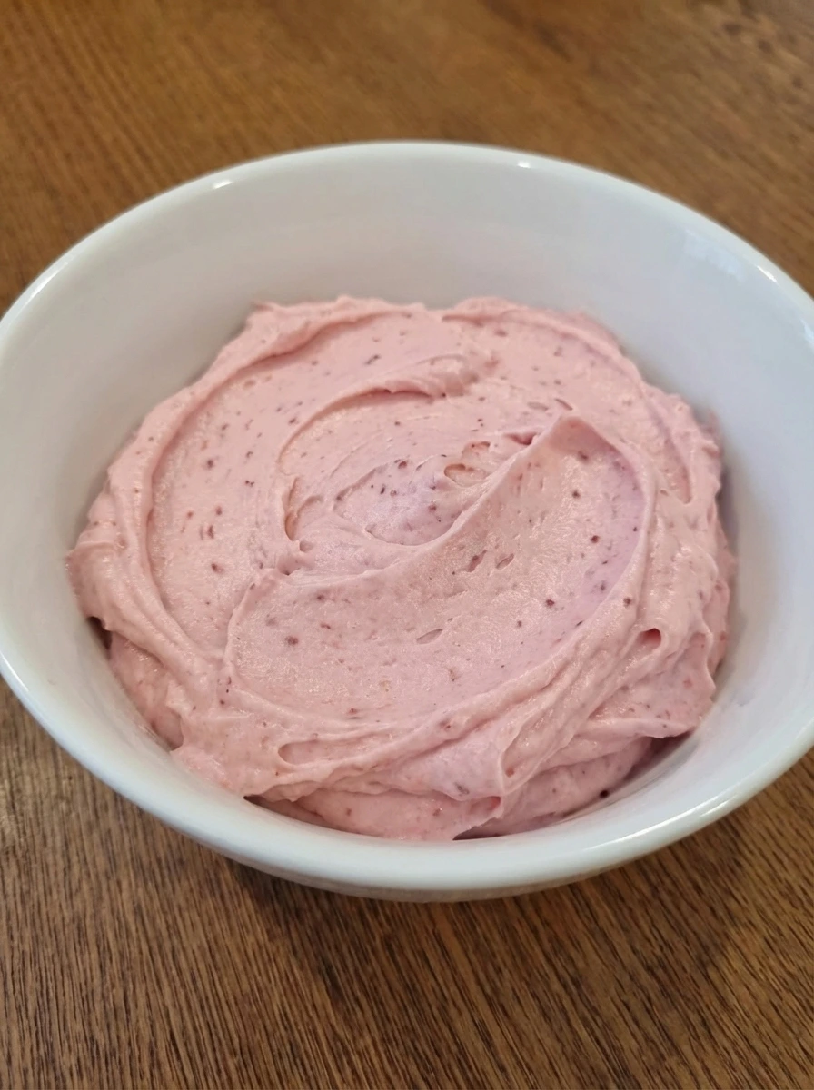 Pale pink strawberry frosting with soft ridges in a white dish