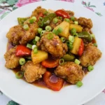 Homemade Sweet and Sour Chicken on a white plate with peppers pineapple and glossy sauce