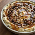 Turtle Cheesecake Dip in a white serving dish with caramel chocolate and pecans.