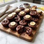 Banana Brownie Bites piled on a wooden board with glossy chocolate chips and fresh banana slices