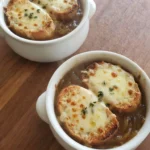 Crockpot French Onion Soup in white crocks with toasted baguette and bubbling Gruyère