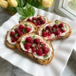Raspberry Ricotta Toast with whipped ricotta, ruby raspberries, balsamic glaze and basil on a white platter