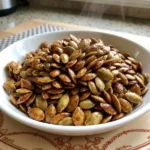 Cinnamon Sugar Roasted Pumpkin Seeds piled in a white bowl with glossy caramelized cinnamon coating