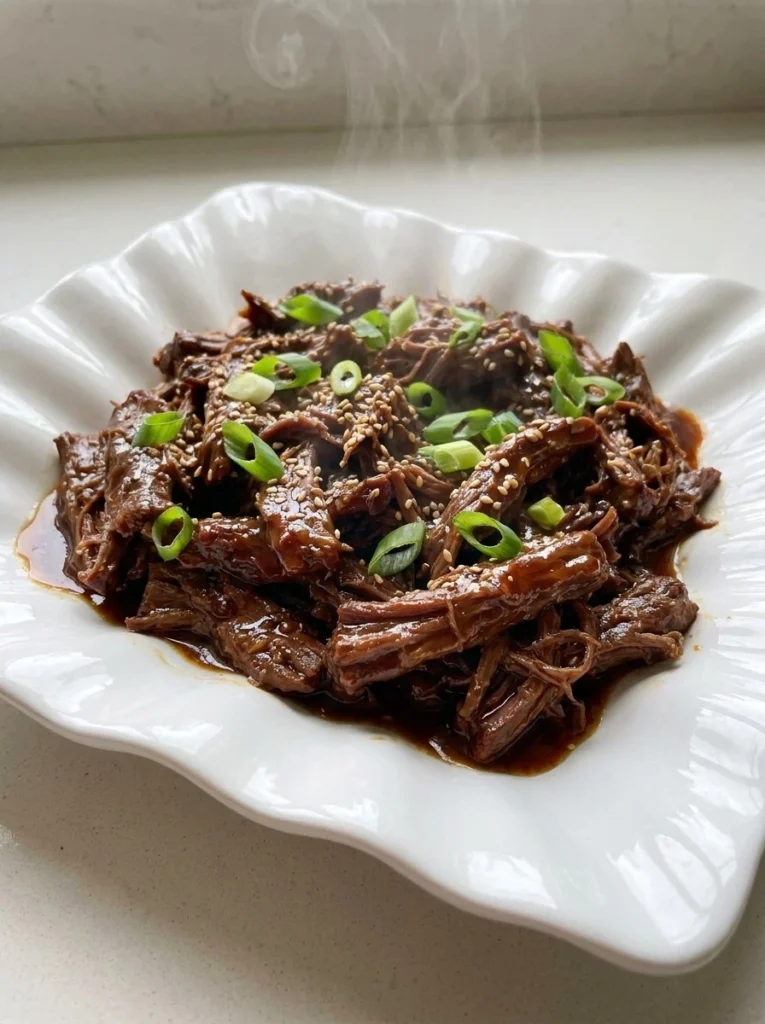 Crockpot Korean BBQ Beef with glossy tender shredded beef and green onion garnish Recipe focus: bbq beef crockpot.
