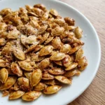 Roasted Pumpkin Seeds with Parmesan piled on a white plate with crisp golden shells and toasted Recipe focus: how to make roasted pumpkin seeds with parmesan.