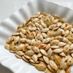 Roasted Pumpkin Seeds with Salt and Pepper piled in a white bowl with golden shells and pepper flecks