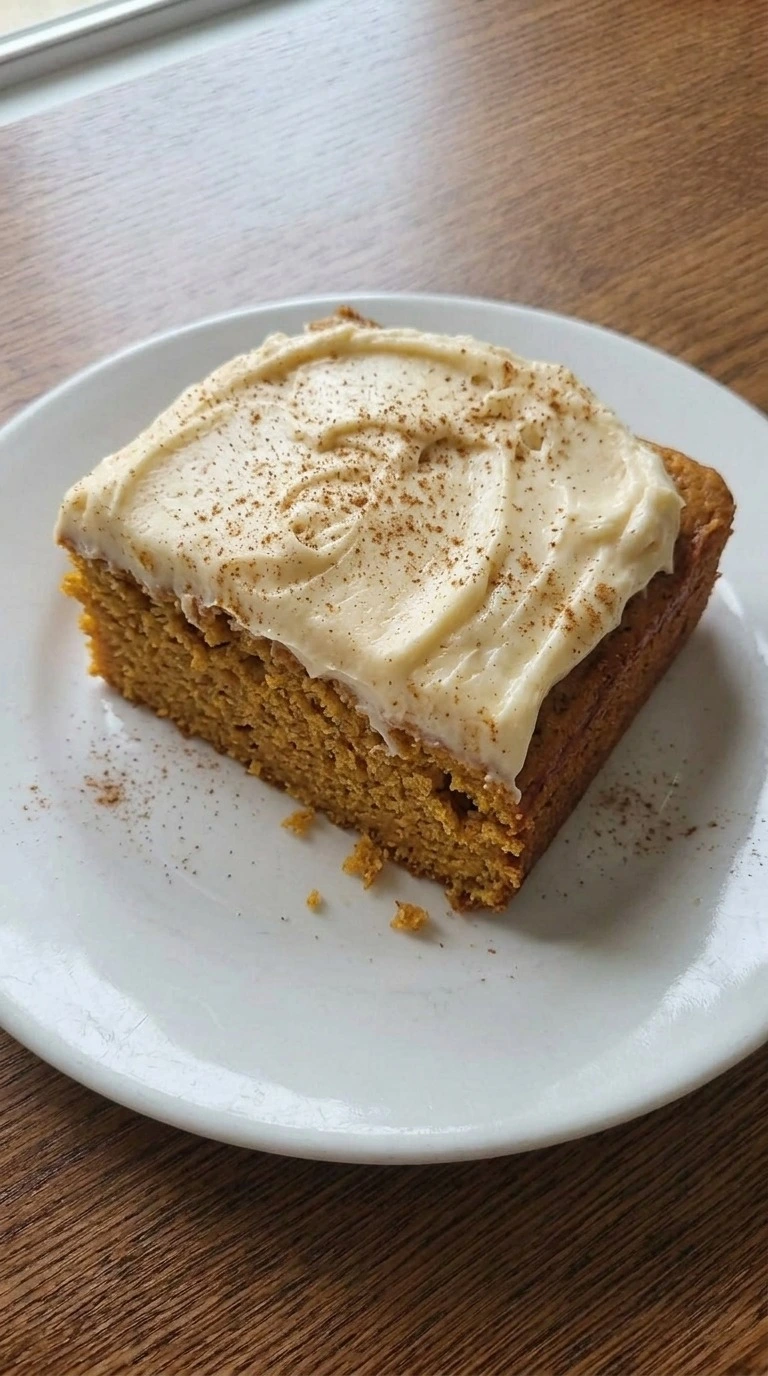 Pumpkin Spice Cake square with cream cheese frosting and a soft orange crumb on a white plate. Recipe focus: pumpkin spice cake recipe.