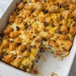 Tater Tot Breakfast Casserole with golden potato tots, melted cheddar and a slice revealing sausage and eggs. Recipe focus: breakfast casserole with hashbrowns.